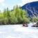 Un grupo de 5 personas con trajes, cascos y chalecos salvavidas practican rafting en un río bordeado de árboles